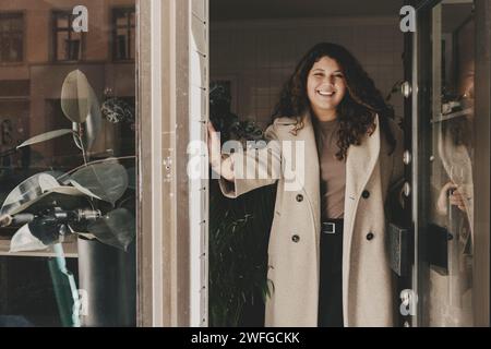 Portrait of smiling businesswoman wearing overcoat while standing near door at office Stock Photo