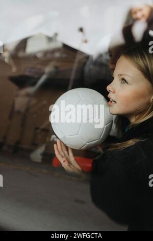 Girl with soccer ball day dreaming seen through glass of car Stock Photo