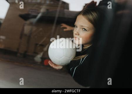 Contemplative girl with soccer ball seen through glass of car Stock Photo