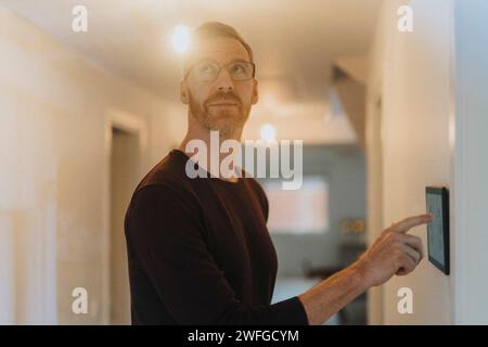 Mature man adjusting room lights through digital tablet while standing at smart home Stock Photo