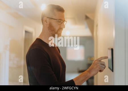 Mature man adjusting room lights through digital tablet mounted on wall at modern home Stock Photo