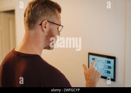 Mature man using digital tablet mounted on wall at smart home Stock Photo