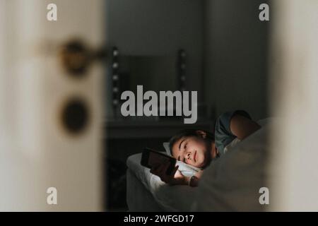 Girl using smart phone while lying on bed in bedroom Stock Photo
