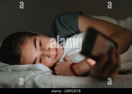 Girl using smart phone while lying on bed at smart home Stock Photo