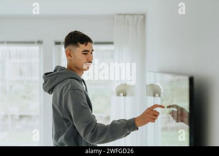 Side view of teenage boy touching smart TV screen in living room Stock Photo