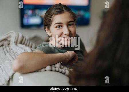 Portrait of smiling girl sitting on sofa by mother in living room Stock Photo
