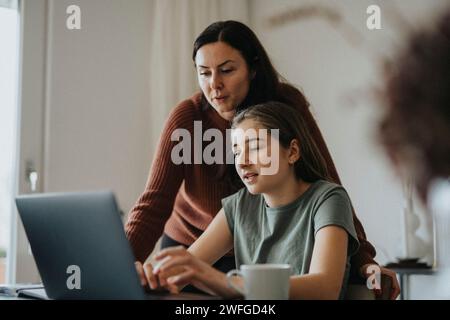 Girl using laptop sitting by mother at modern home Stock Photo
