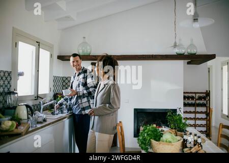 Happy friends talking while standing together in kitchen at home Stock Photo