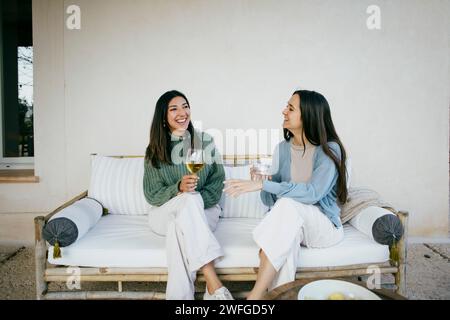 Happy female friends talking while sitting with drinks in backyard Stock Photo