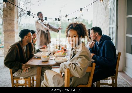Portrait of happy young woman sitting at dining table with friends during dinner party Stock Photo