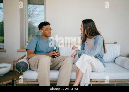 Young man and woman with drinks sitting on sofa in patio Stock Photo