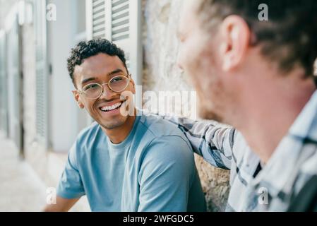 Smiling male friends talking while sitting at backyard Stock Photo