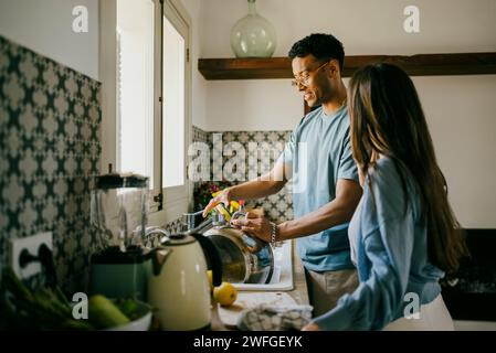 Young man and woman washing dishes together in kitchen sink at home Stock Photo