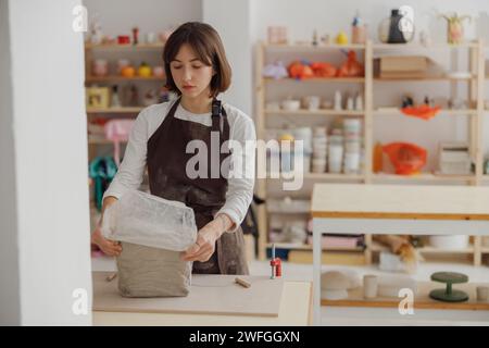 Ceramist woman wearing apron is preparing clay to make pottery pieces in her studio Stock Photo