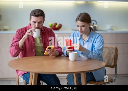 Married couple addicted to smartphones sitting at home, reading news online, surfing in internet Stock Photo