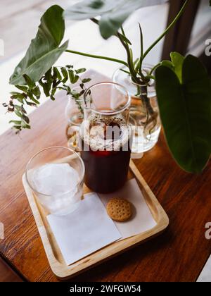 Hand pouring coffee cold brew espresso ice coffee with ice cubes. Glass cold brew coffee with ice on morning light wooden table background. Stock Photo