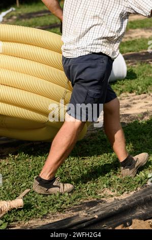 Workers carry a roll of yellow drainage pipe in their hands. Preparation for drainage works and removal of groundwater. Stock Photo