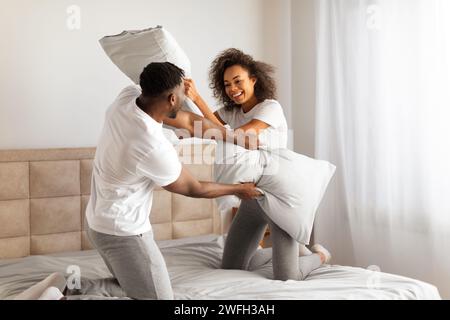 Playful african spouses having fun in bedroom enjoying pillow fight Stock Photo