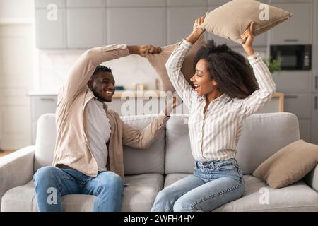 Joyful Black Millennial Couple Having Pillow Fight In Living Room Stock Photo