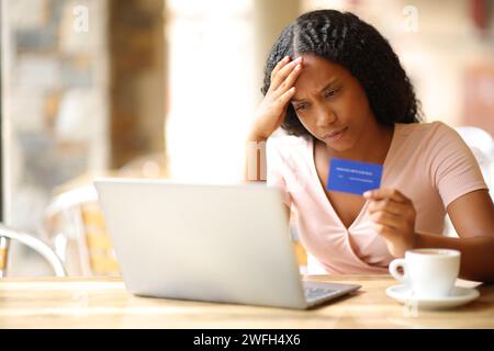 Worried black woman having problem buying online in a coffee shop terrace Stock Photo
