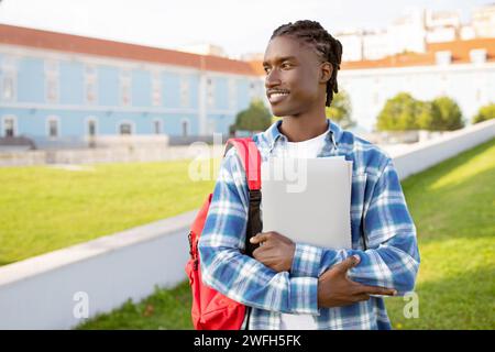 Black student guy hugs laptop standing with backpack near university Stock Photo