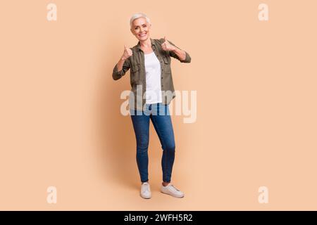 Full length photo of lovely pensioner lady show double thumb up dressed stylish khaki garment isolated on beige color background Stock Photo