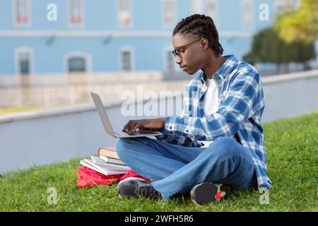 Focused black guy engages in e-learning on his laptop outdoor Stock Photo