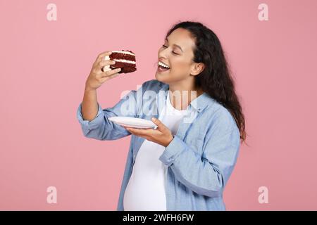 Excited Pregnant Lady Eating Cake Standing Over Pink Studio Background Stock Photo