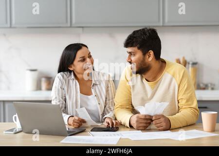Smiling indian couple with laptop in kitchen calculating bills Stock Photo