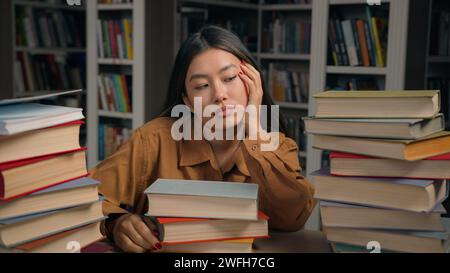 Sad tired woman girl student bored at desk with books in university library lazy unmotivated asian female preparing for difficult college exam Stock Photo