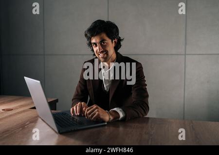 Portrait of happy professional business man company executive ceo manager wearing suit sitting at desk in office working on laptop computer smiling at Stock Photo