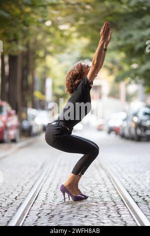 woman in high heels performing yoga on street Stock Photo