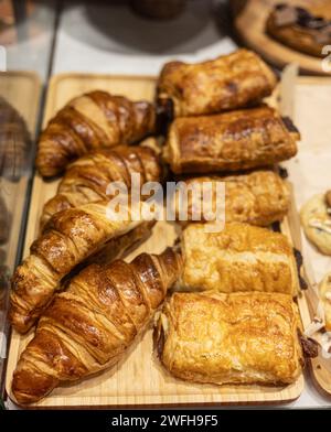 Golden croissants and assorted pastries displayed on a wooden tray in a bakery case. Stock Photo