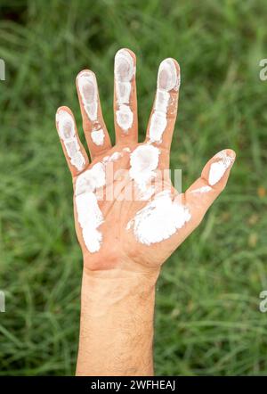 close up of man's hand covered with white paint on the green grass background. preservation of the environment concept Stock Photo