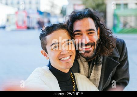 Happy gay couple smiling while taking selfies together outdoors. Stock Photo