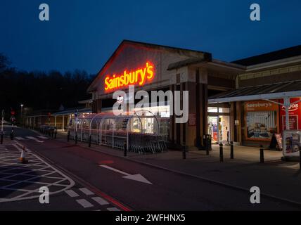 Sainsbury supermarket entrance and trolley park at Torquay, Devon, England. Night time photography illuminated and lit up. Stock Photo