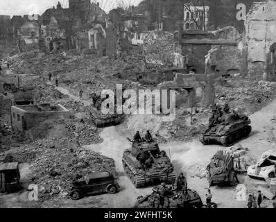 Watched by young children, American tanks and troops patrol the devestated city streets of Nuremberg on the 20th April 1945, during the final days of the Second World War. Stock Photo