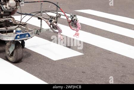 City workers paint crosswalk lanes on the road with painting machine. Close up. Stock Photo