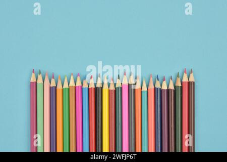 A group of seamless wooden coloured pencils placed in a row facing up isolated on blue background Stock Photo