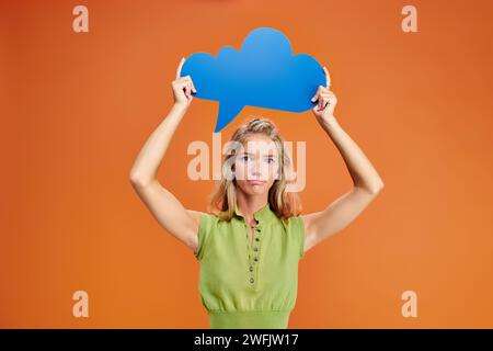 confused adolescent girl in everyday outfit holding thought bubble above head and looking at camera Stock Photo