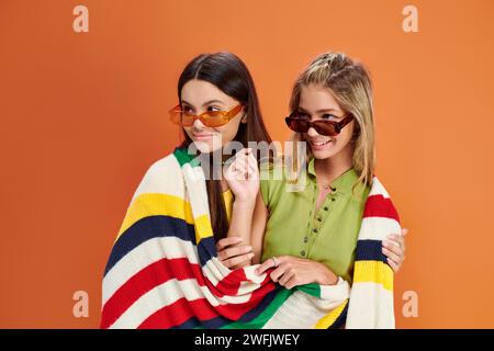 joyous adorable teens with sunglasses covering with blanket and looking away, friendship day Stock Photo