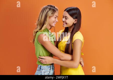 joyous adorable teenage girls in casual attires hugging and smiling at each other, friendship day Stock Photo