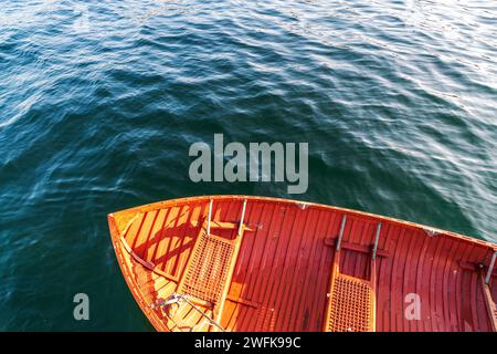 A small red-orange rowboat surrounded by tiny fish rests in the dark green water of Penn Cove at Coupeville, Whidbey Island, Washington. Stock Photo