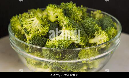 A glass bowl with raw organic broccoli florets close-up on black background Stock Photo