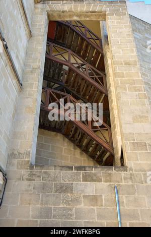 A unique view of a wooden staircase through an open window in a historic stone building in Jerez de la Frontera Stock Photo