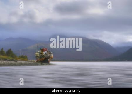 The old boat of Caol or the Corpach Wreck rests on the shore where Loch Linne and Loch Eil meet on the Scottish west coast. View up to Ben Nevis. Stock Photo