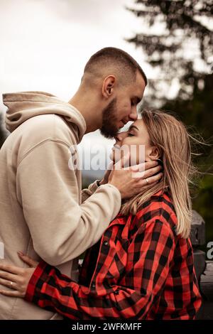 Young man and woman in love standing at observation deck somewhere in mountains looking at landscape Stock Photo