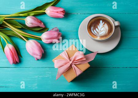 Pink tulips, a cup of cappuccino and gift in a box on a turquoise wooden table. Spring festive background, top view, flat lay. Stock Photo