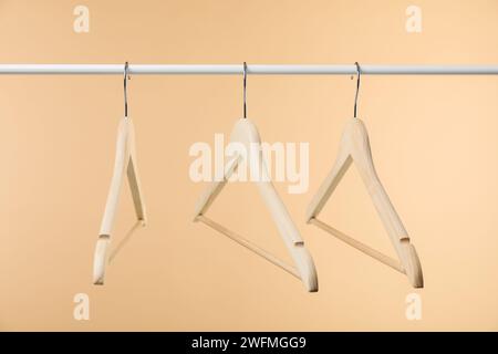 Empty clothes hangers on wooden rack against beige background Stock Photo