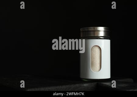 Salt shaker on wooden board against black background. Space for text Stock Photo